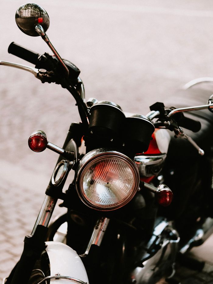 Close-up of a vintage motorcycle parked outdoors on a cobblestone street, highlighting the headlight and handlebars.