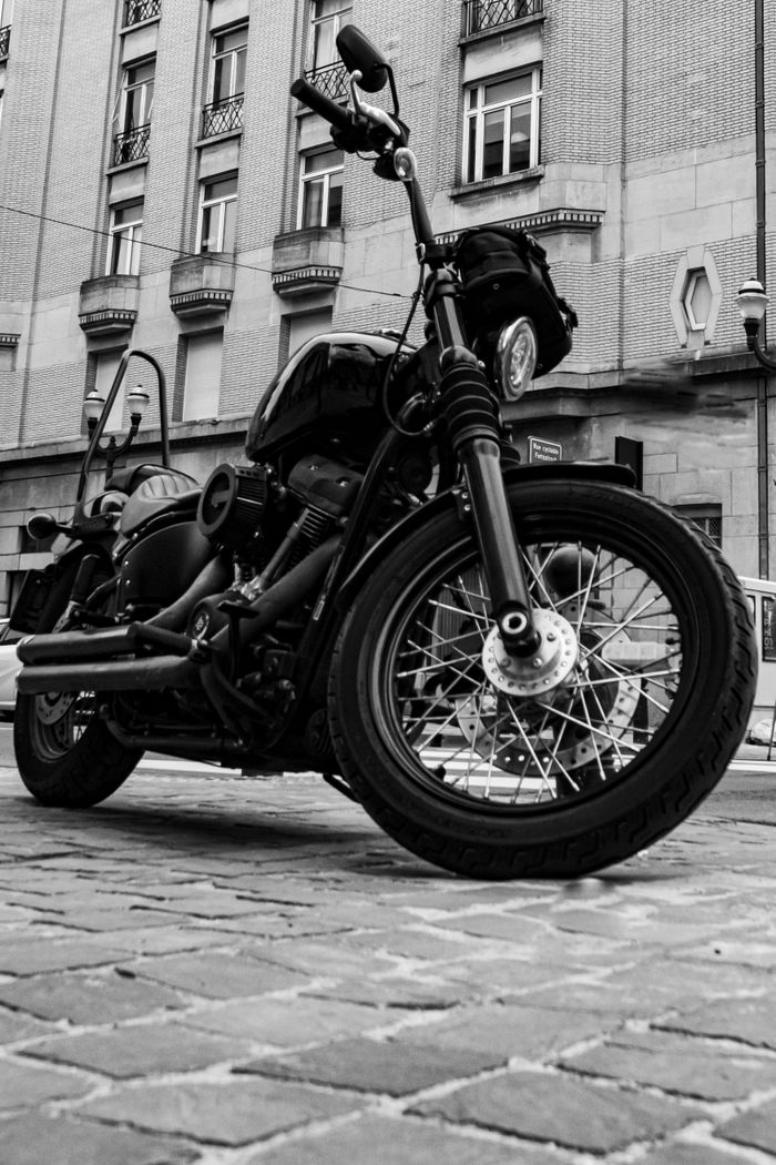 A parked motorcycle in a city street, pictured in black and white, showcasing urban architecture.